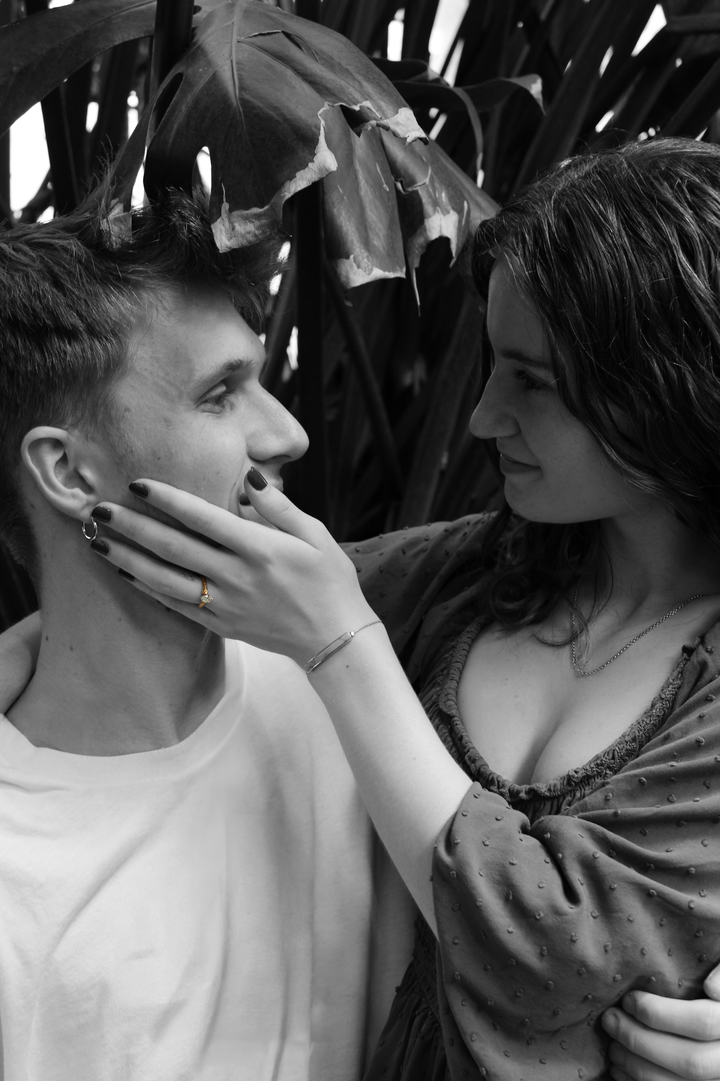 A woman and a young man looking at each other closely, with the woman touching the man's chin, in a black and white photo.