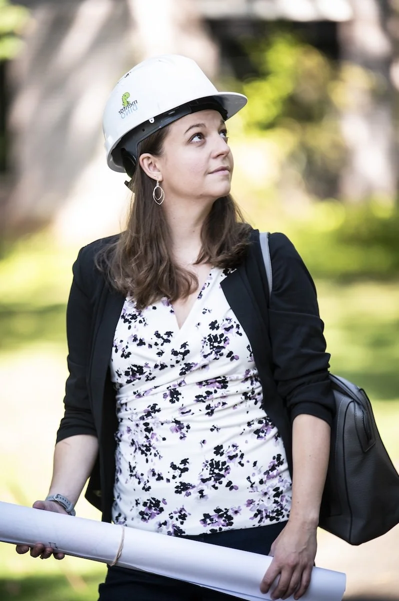 Katelyn in a hard hat with a roll of drawings looking up