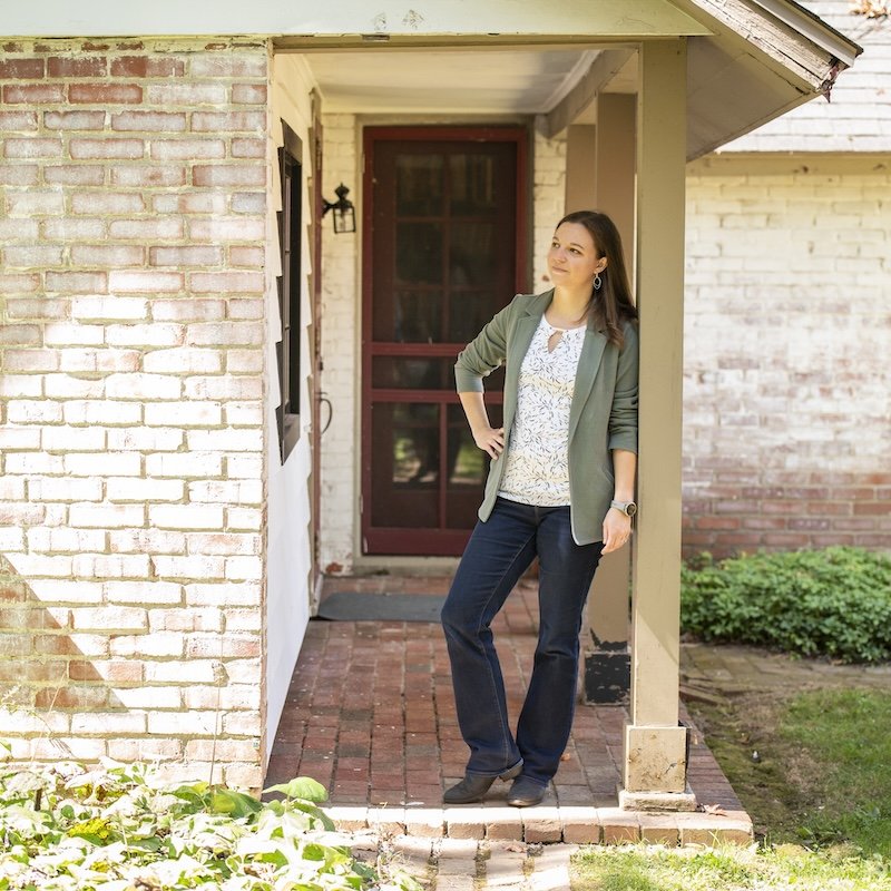 Katelyn leaning on a column on a front porch in the sunshine