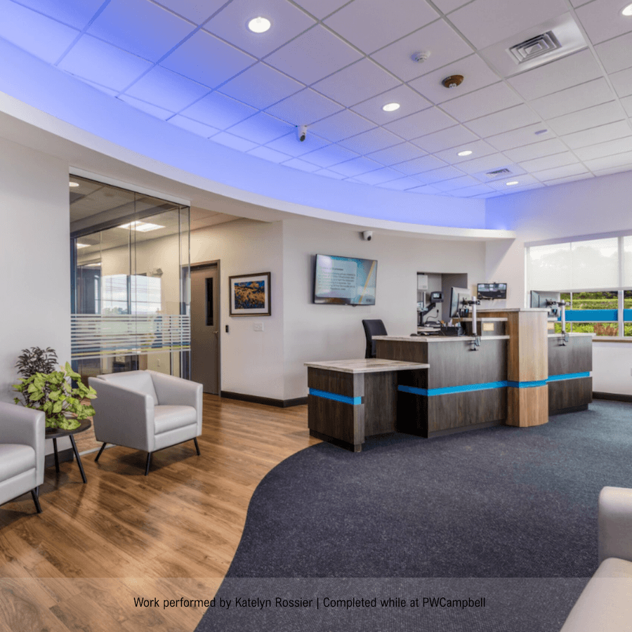 A modern office lobby with seating area, front desk, computer monitors, and a television on the wall, featuring wood and white decor with blue accent lighting.