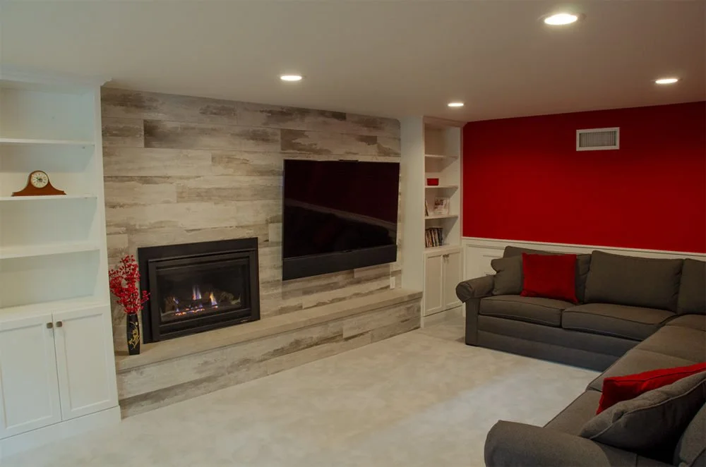 Finished basement family room with a gas fireplace, wood-look tile surround and built-in shelving