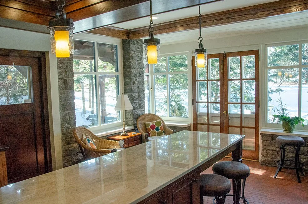 Kitchen island with a granite countertop and amber pendants beside a sunroom with stone columns