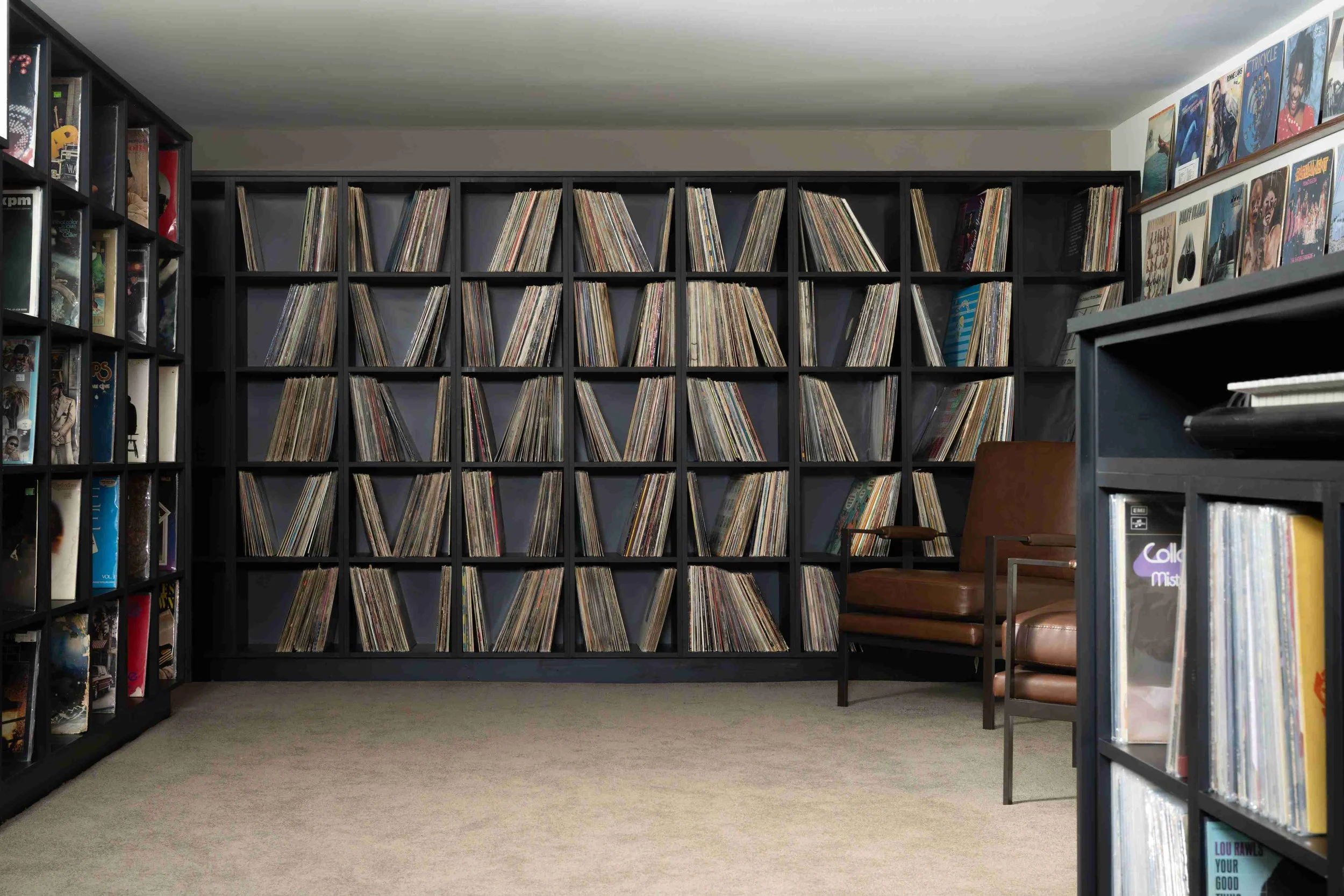 Custom floor-to-ceiling vinyl record storage wall with leather armchair, Minneapolis basement
