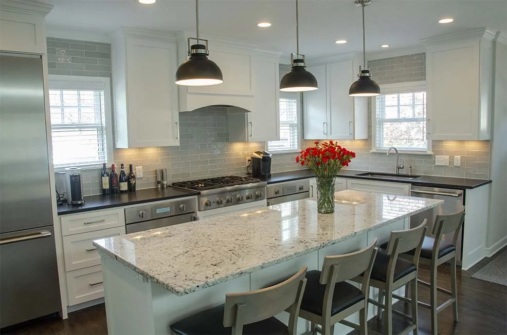 White kitchen with a granite island, black pendant lights and a gray subway tile backsplash