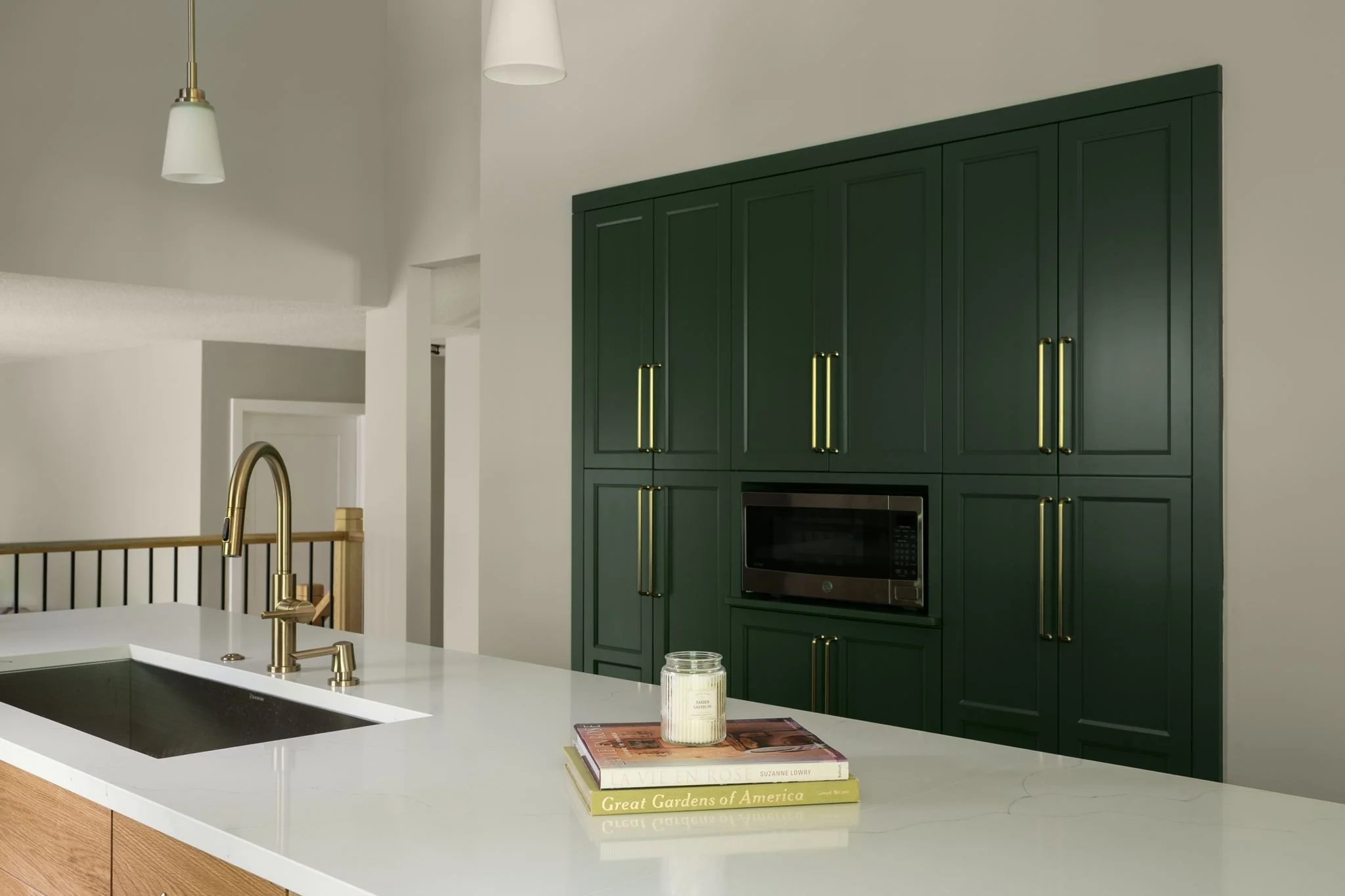 White quartz kitchen island with taper candles
and brass pendant light, dark green kitchen cabinetry, Eden Prairie remodel