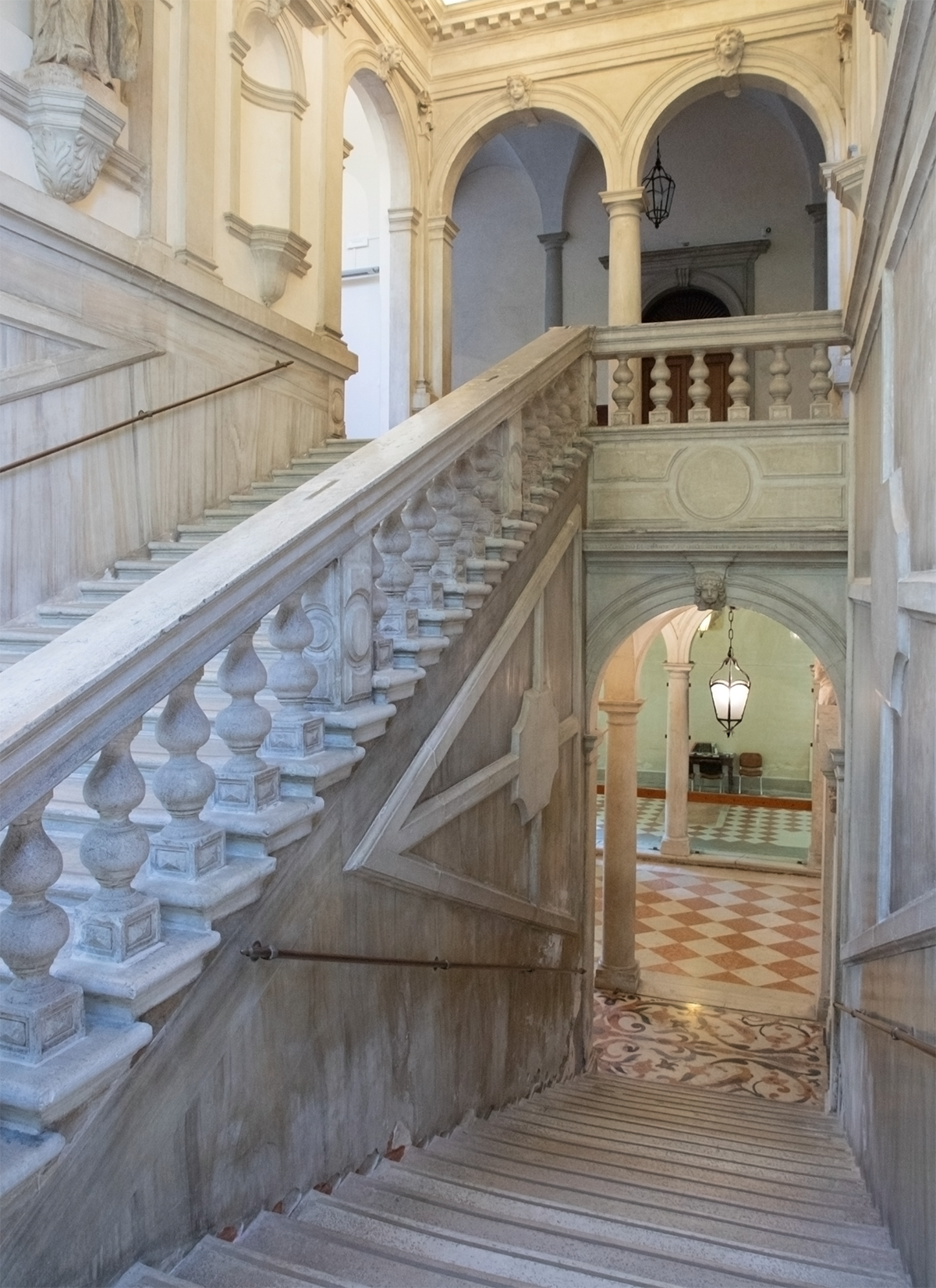 Elegant marble staircase with decorative balustrades in a grand historical building, featuring arches and classical architectural details.