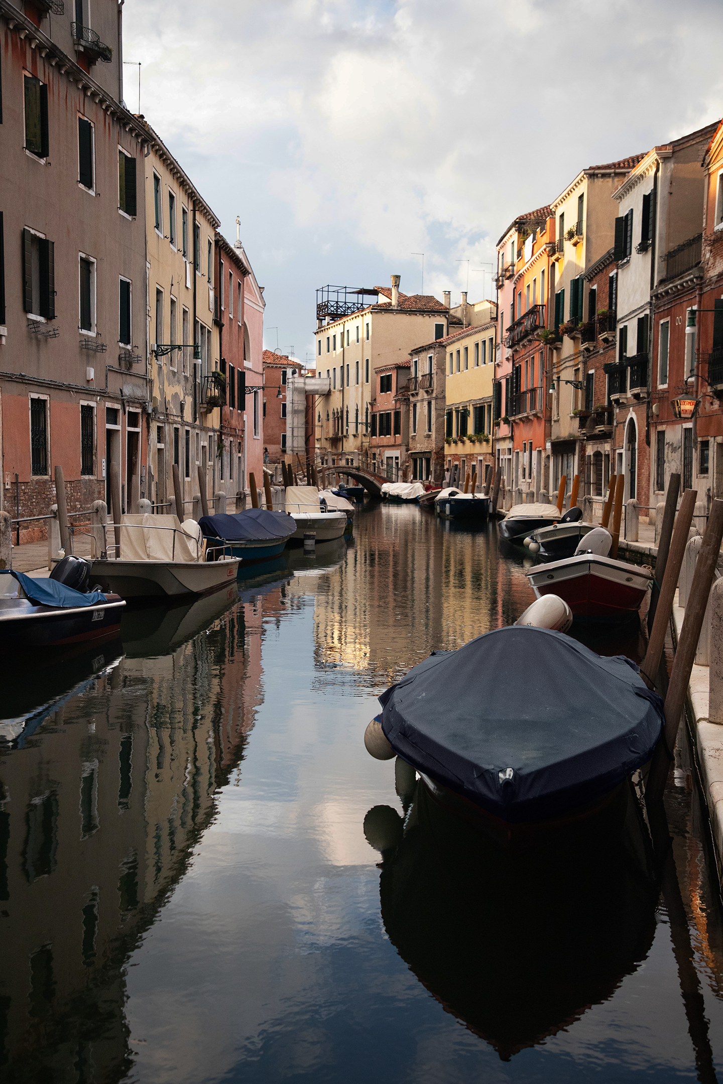 Colorful buildings along a narrow water canal with boats docked on the sides, reflecting the cloudy sky.
