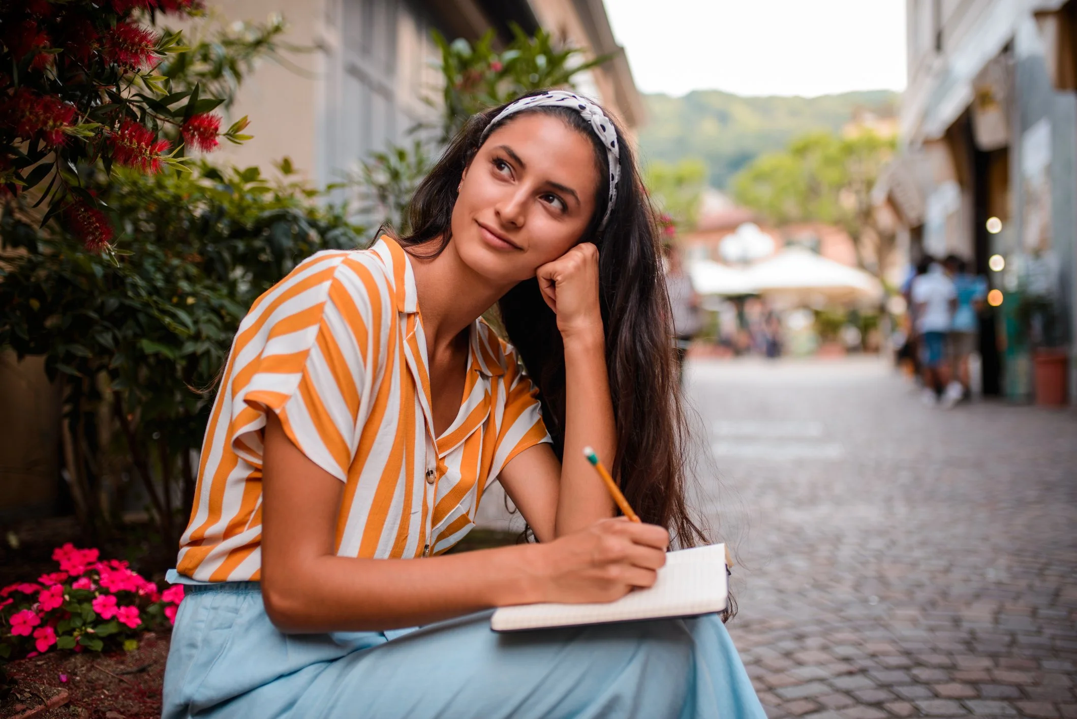 young woman journaling while sitting on a step near a cobblestone street