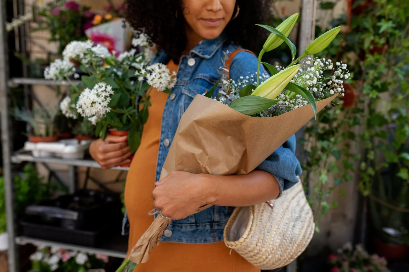 pregnant woman of color in a jean jacket holding flowers at a market