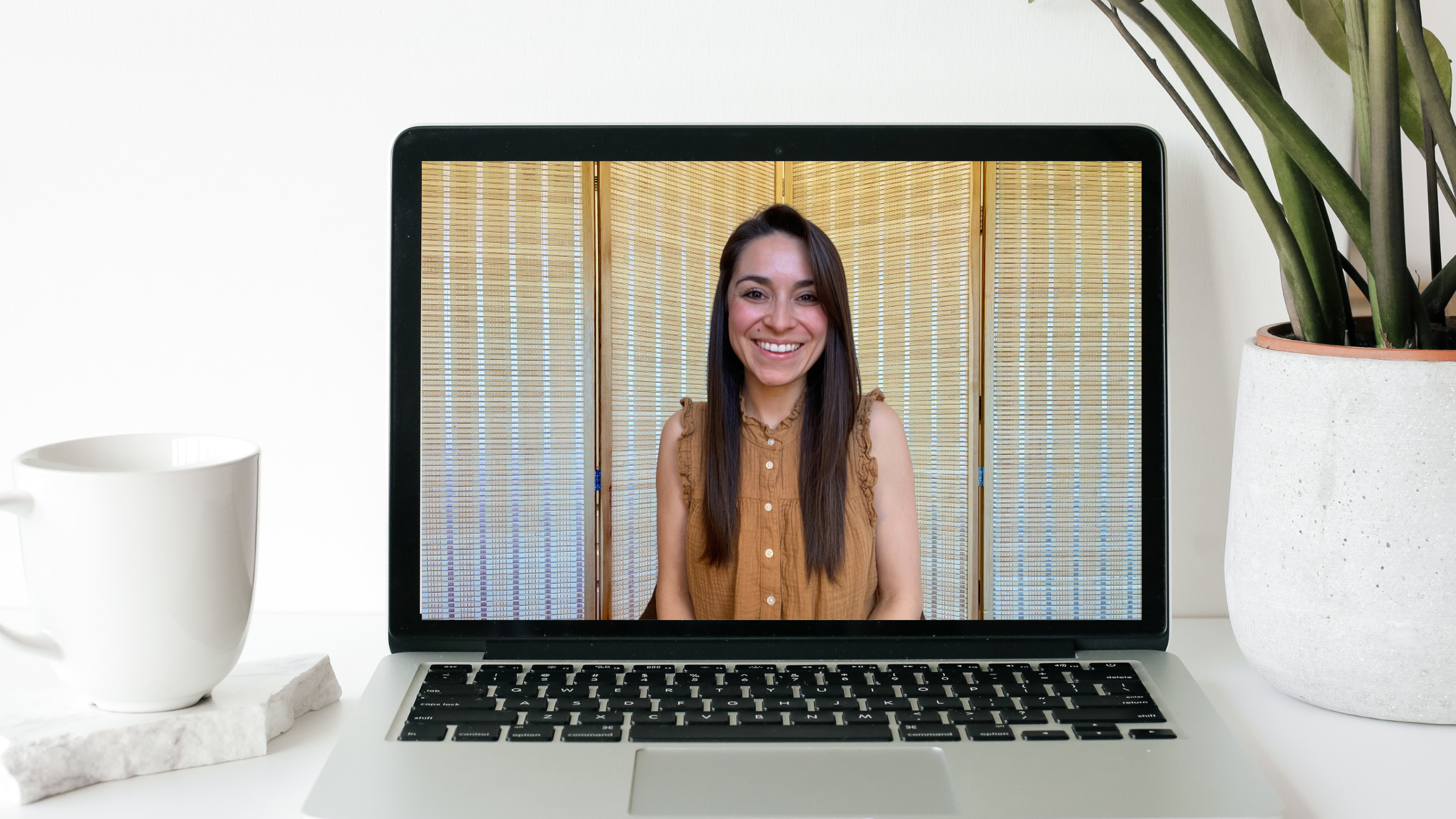 Kayti McDaniel, seen on a laptop with a white mug and green plant close by