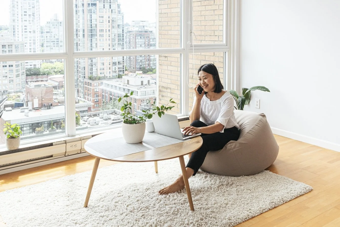 a woman smiling while speaking on her cell phone and sitting on a large beanbag in front of her open laptop