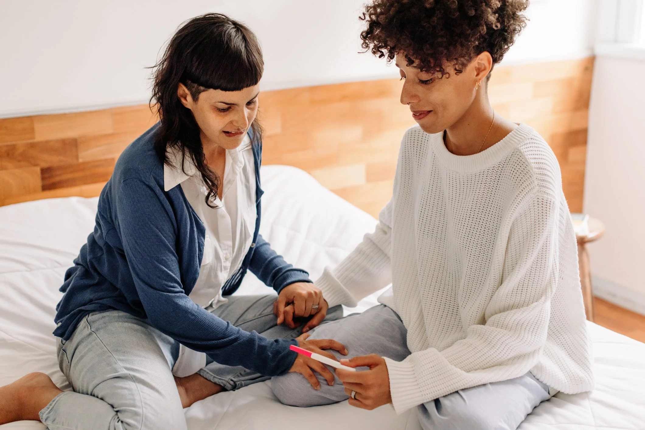 a lesbian couple sitting on their bed holding hands waiting for the results of a pregnancy test