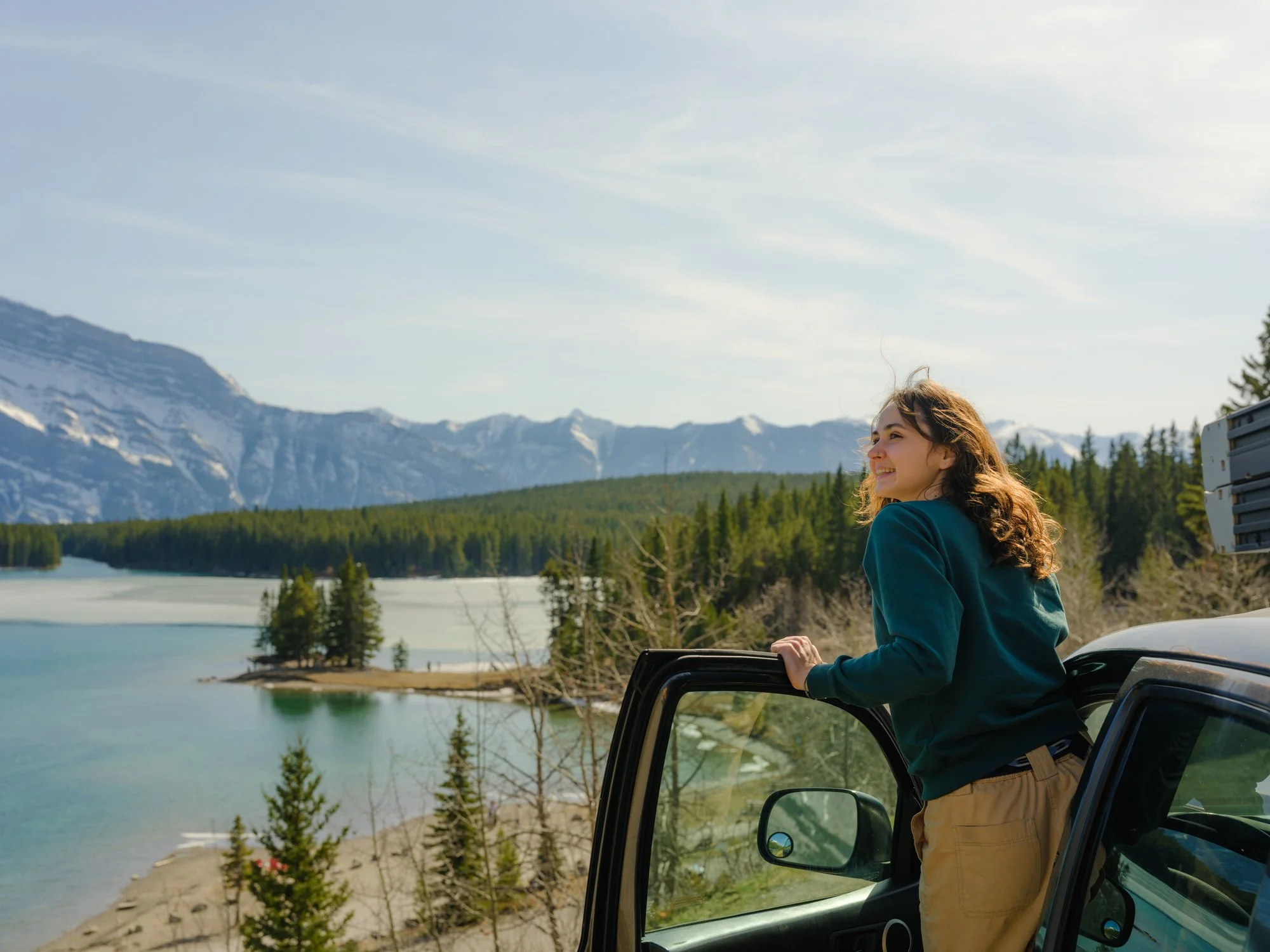 a young woman smiling while leaning out of her car to see a beautiful landscape