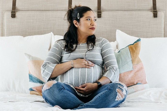 a pregnant woman of color holding her belly and looking off into the distance