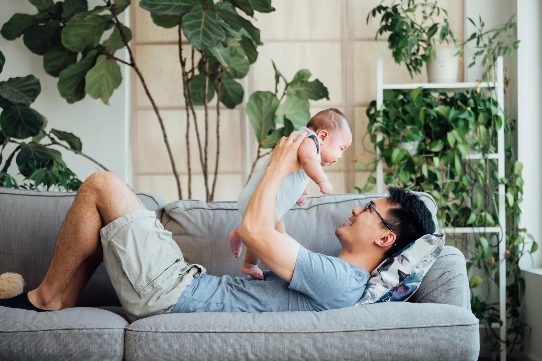 a new father laying on a sofa, holding and smiling at his baby overhead