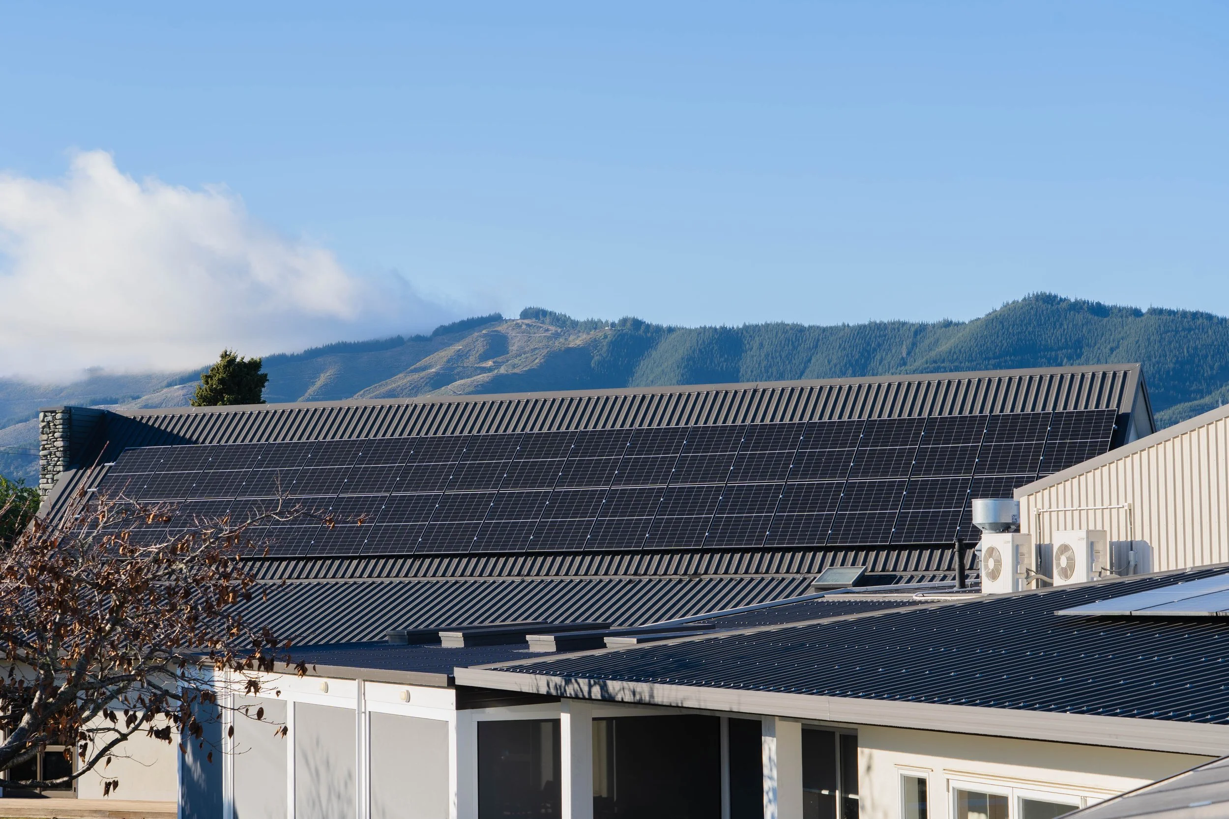 Commercial building with solar panels on the roof installed by Rowan Dron Electrical, situated in a mountainous area with a blue sky and a few clouds