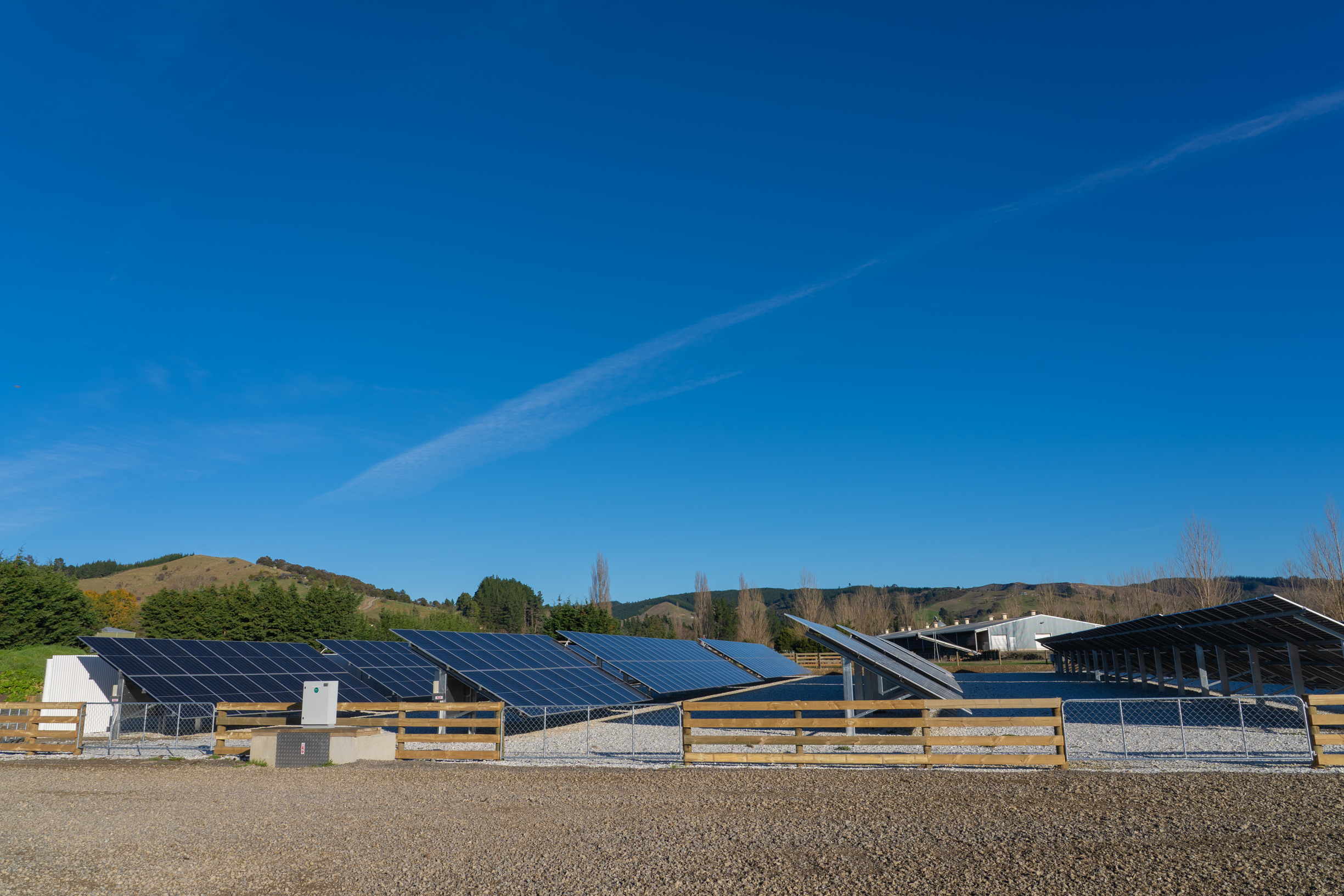 Solar panels installed on a property with a fence and mountainous landscape in the background under a clear blue sky.