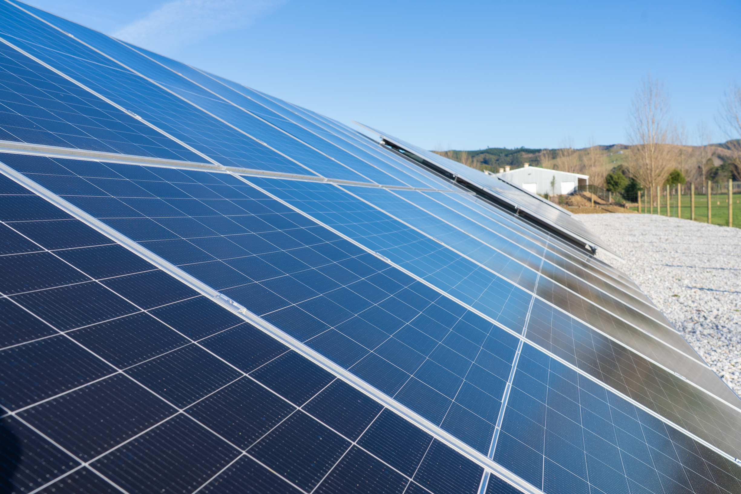 Close-up of blue solar panels installed outdoors with a rural landscape and clear sky in the background.