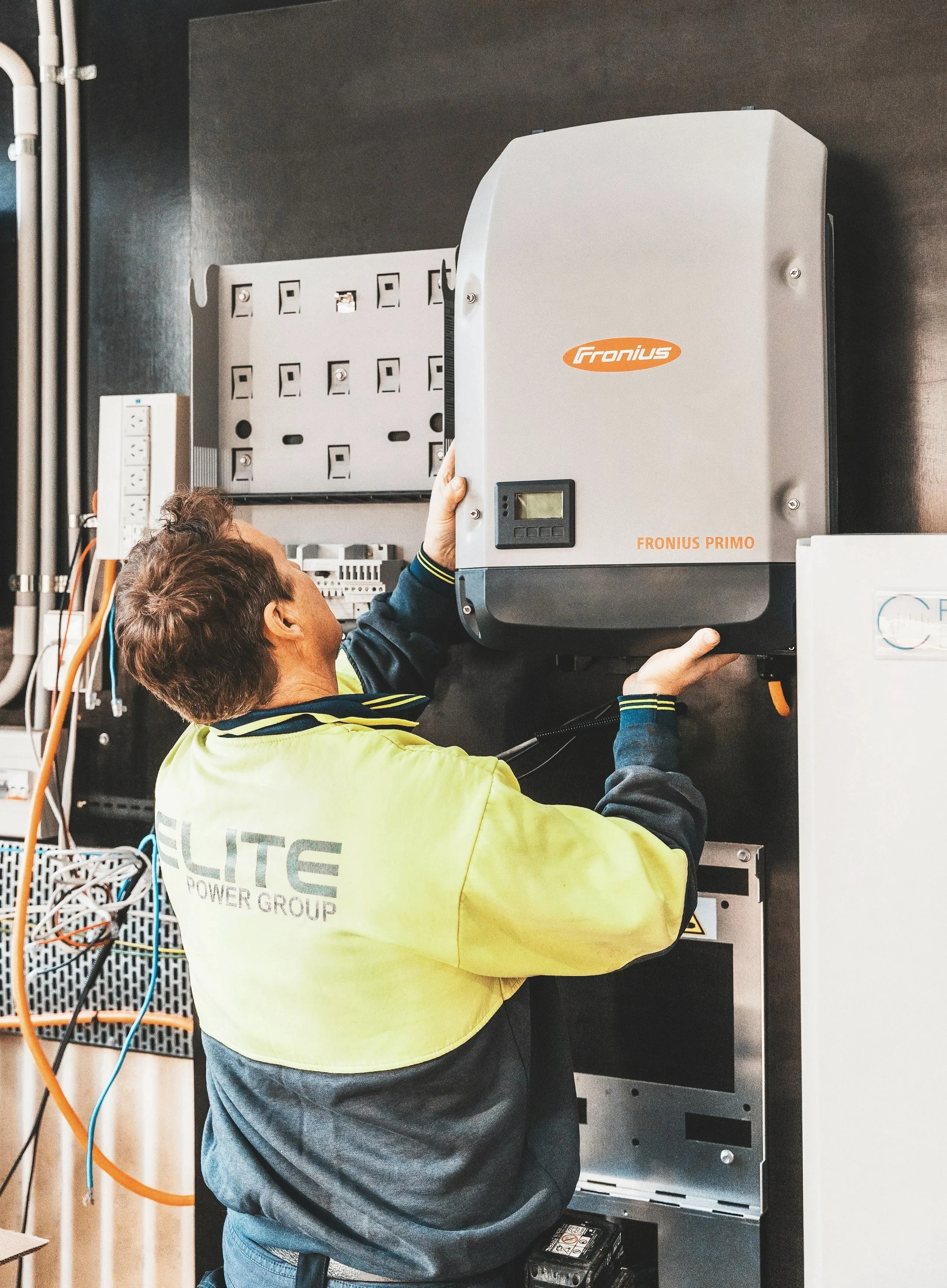 A man wearing a yellow vest working on an electrical panel.