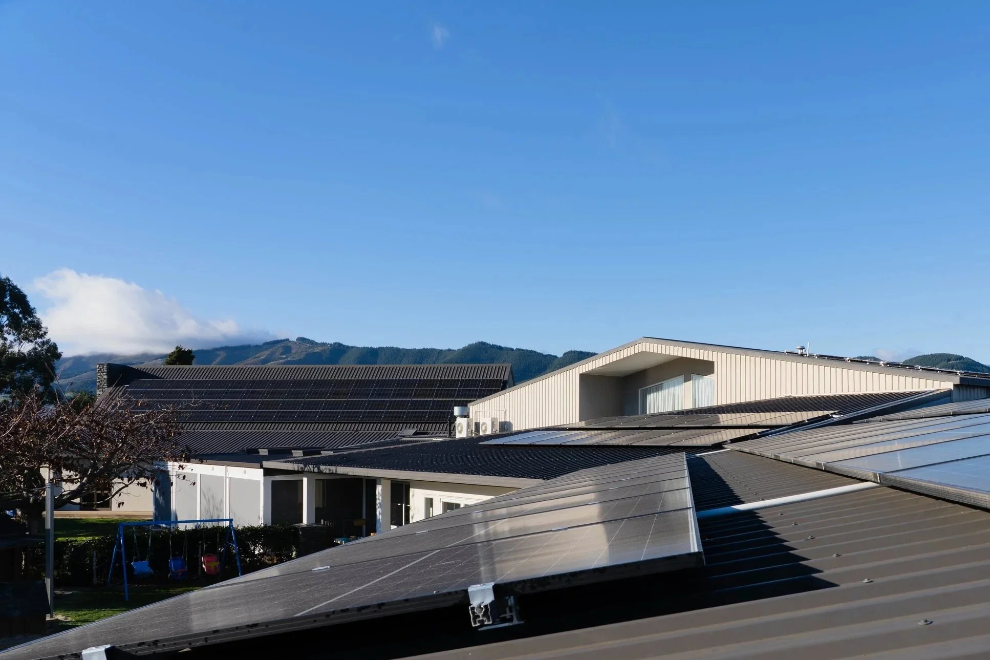 Residential rooftops with solar panels under a clear blue sky, mountains in the background.