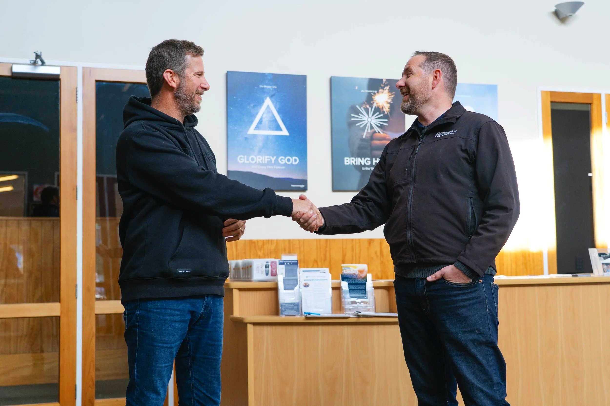 Rowan and a client shake hands and smile at each other inside a room.