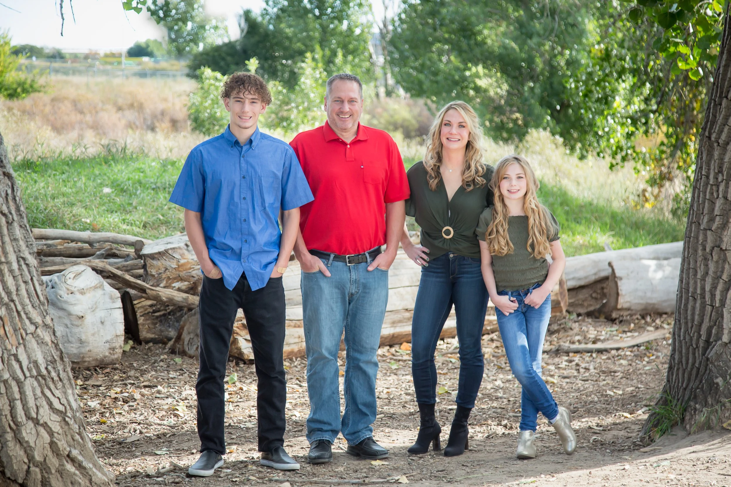 A family of four standing outdoors under trees, smiling at the camera.