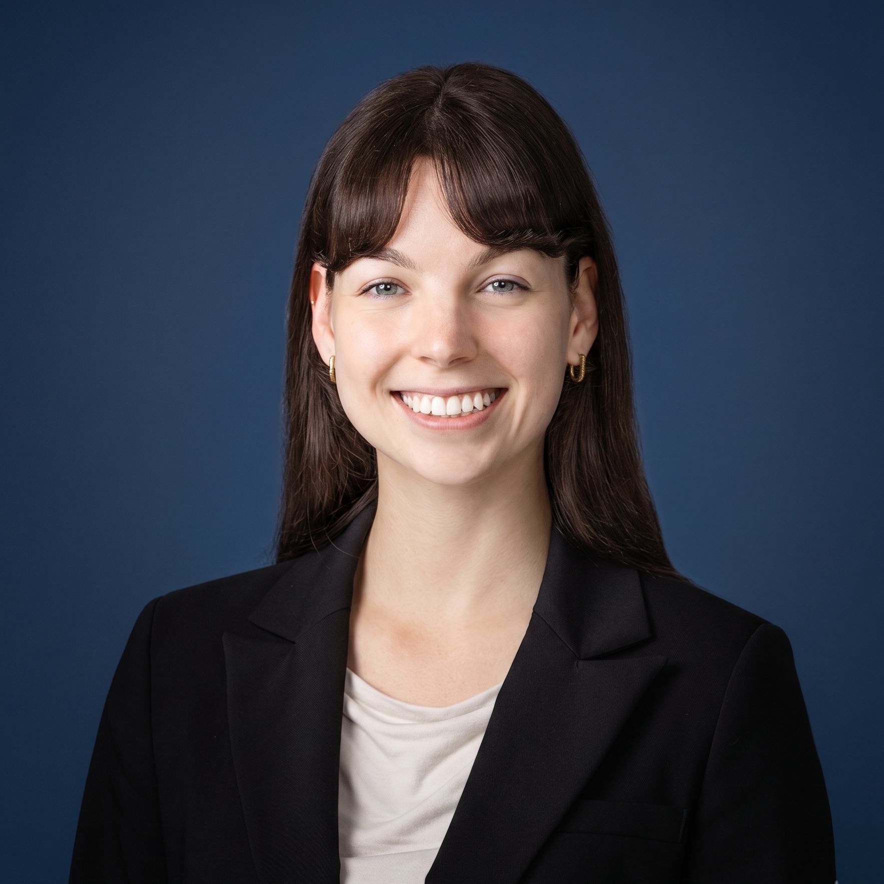 Portrait of a smiling woman with dark brown hair, wearing a black blazer and a white top, against a dark blue background.