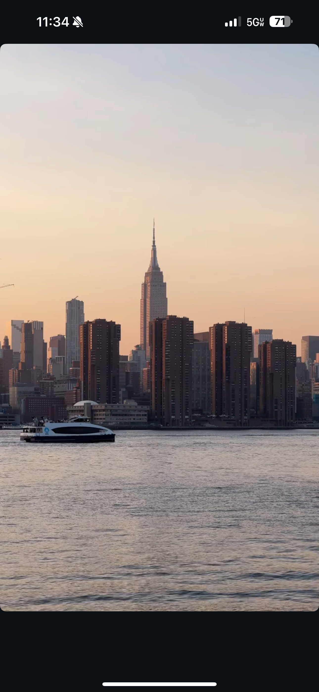 View of Manhattan skyline featuring the Empire State Building at sunset, across a river with a boat in the foreground.