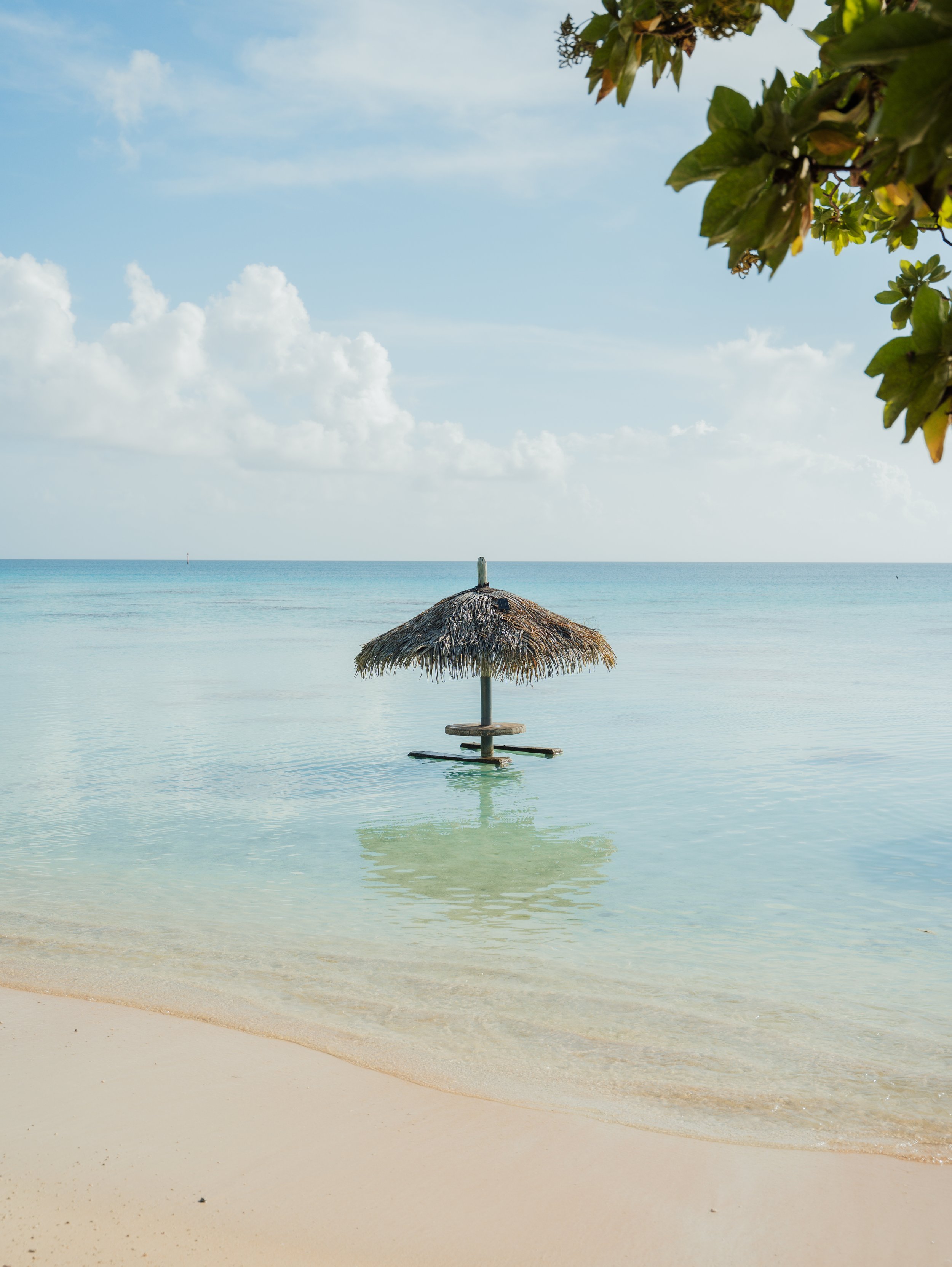 Une cabane de paille sur la plage, à Fakarava une étendue d'eau calme, un ciel nuageux et une végétation verdoyante en haut à droite.