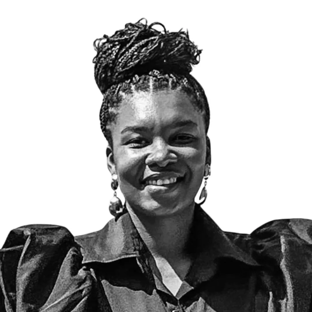 Portrait d'une femme afro-américaine souriante avec des cheveux en dreadlocks enroulés en haut, portant des boucles d'oreilles et un vêtement à manches bouffantes, en noir et blanc.
