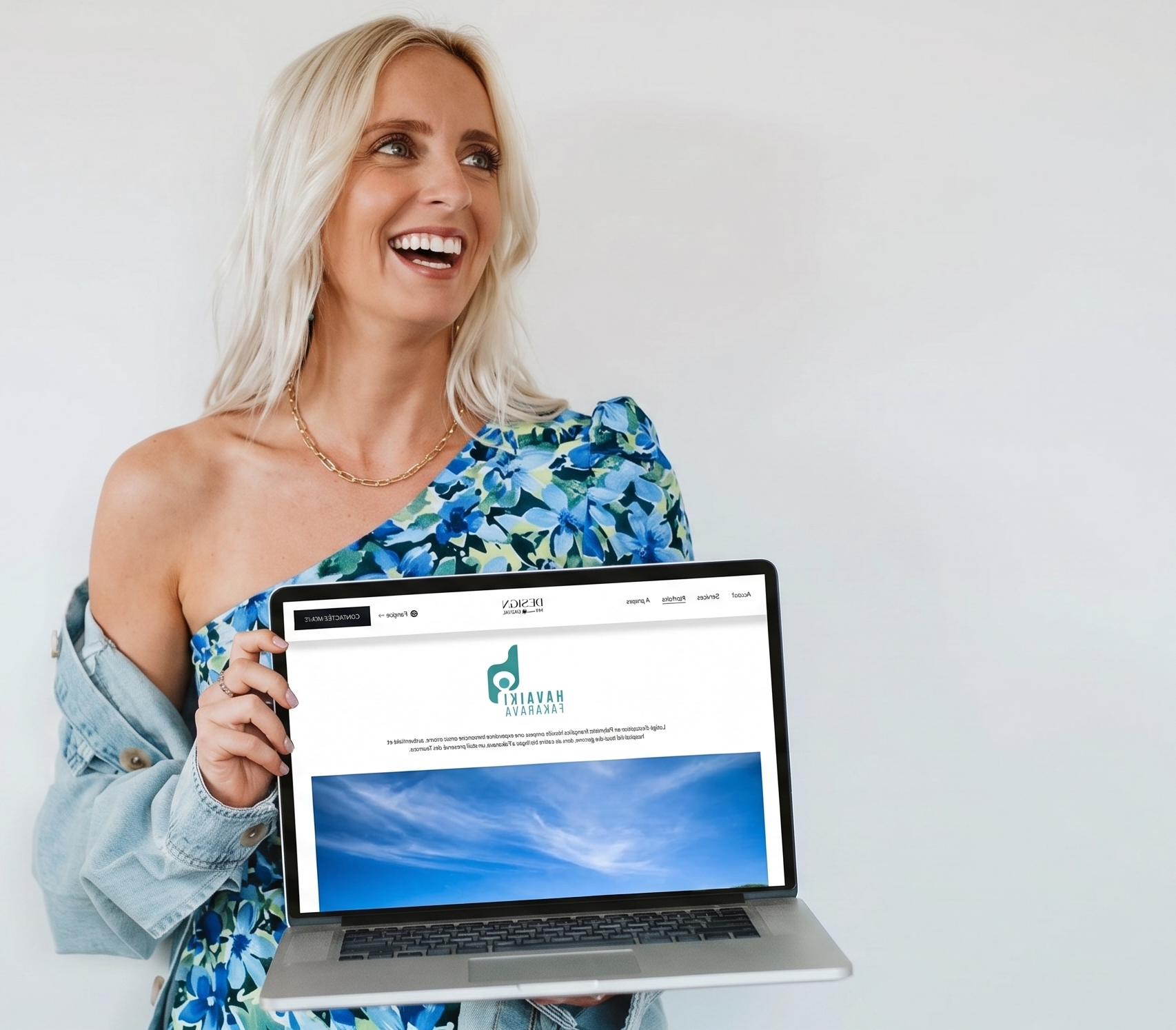 Jeune femme souriante tenant un ordinateur portable affichant un site web avec un fond de ciel bleu et de nuages, habillée d'une robe fleurie et d'une veste en jean, portant un collier doré.