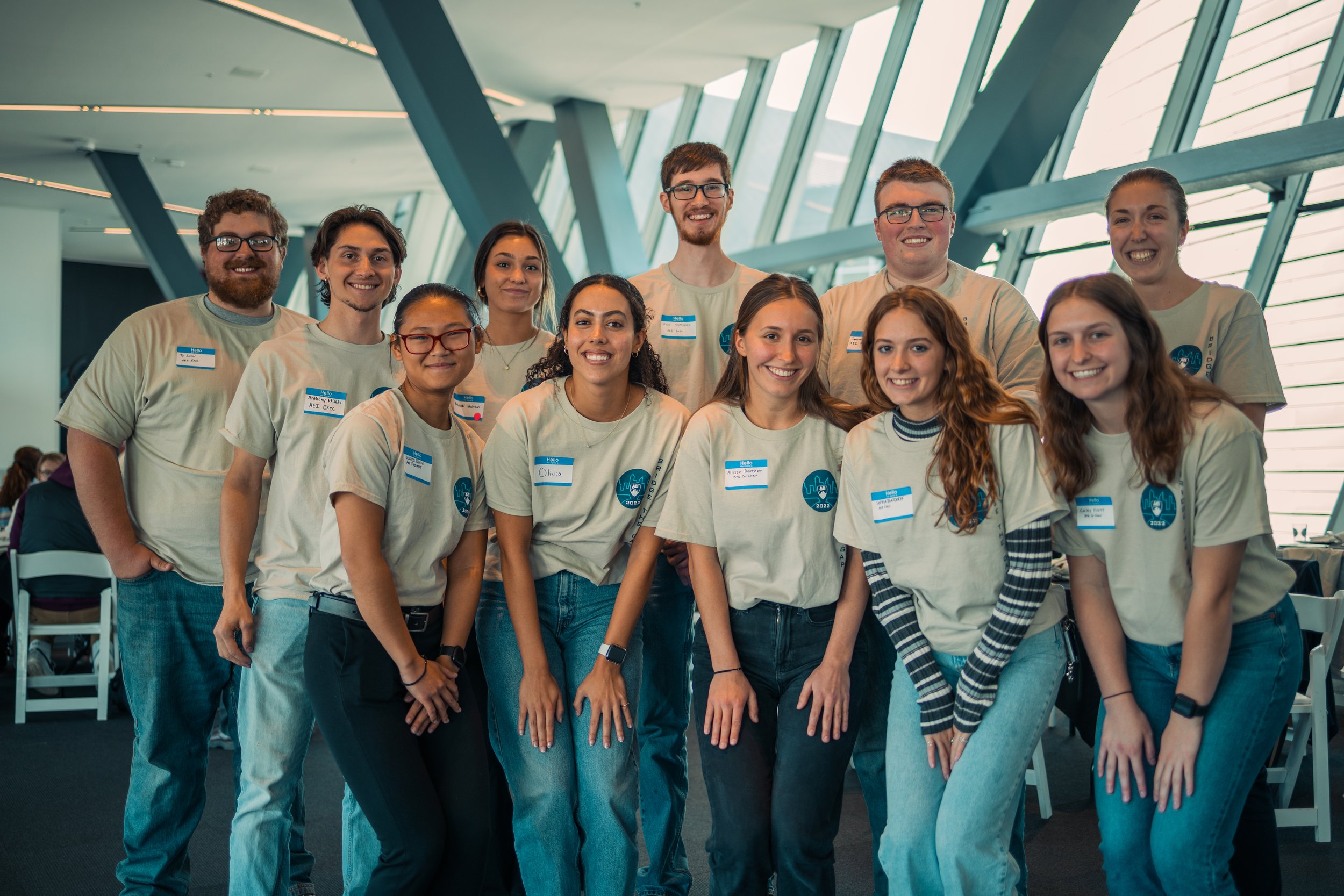 A diverse group of young adults smiling at the camera at an indoor event with large windows and modern architecture.