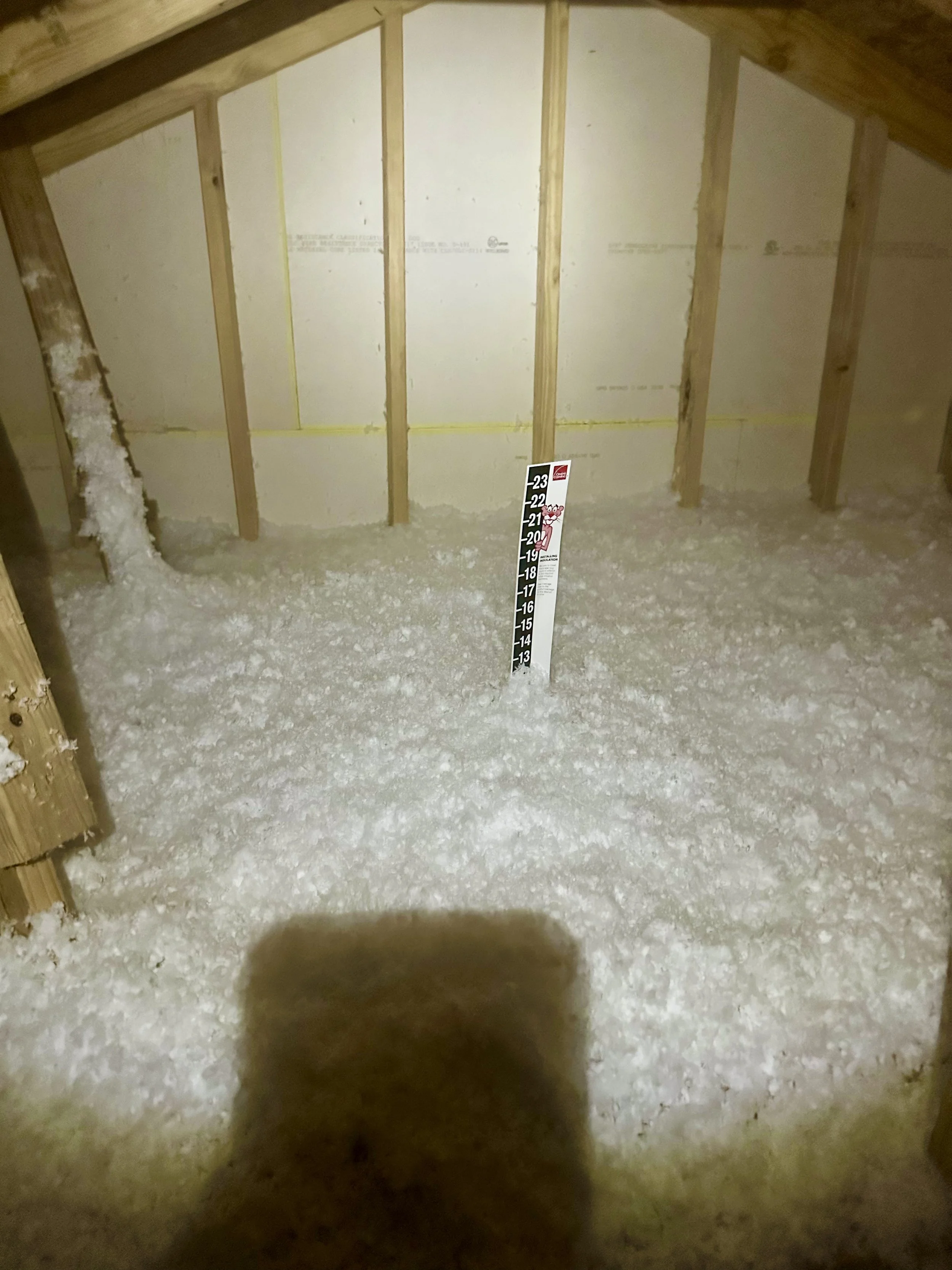 A construction area with exposed wooden framework and drywall insulation, a height measurement stick at approximately 20 feet, and insulation in the attic. insulation install job site