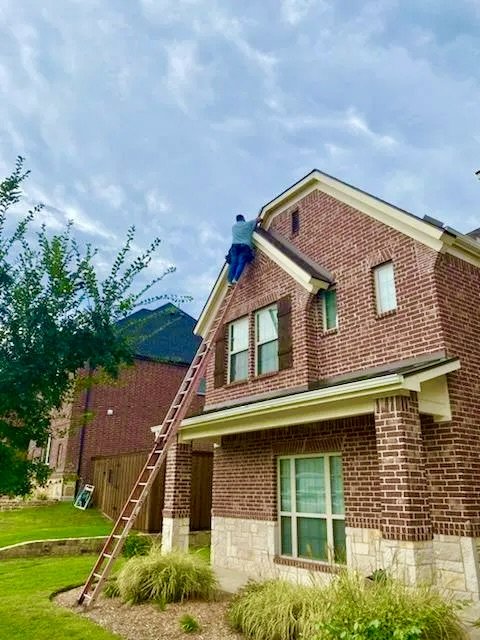 A person working on the roof of a brick house using a long ladder in a suburban neighborhood. performing rodent exclusion, rat, squirrel, raccoon, possum, bird, bat