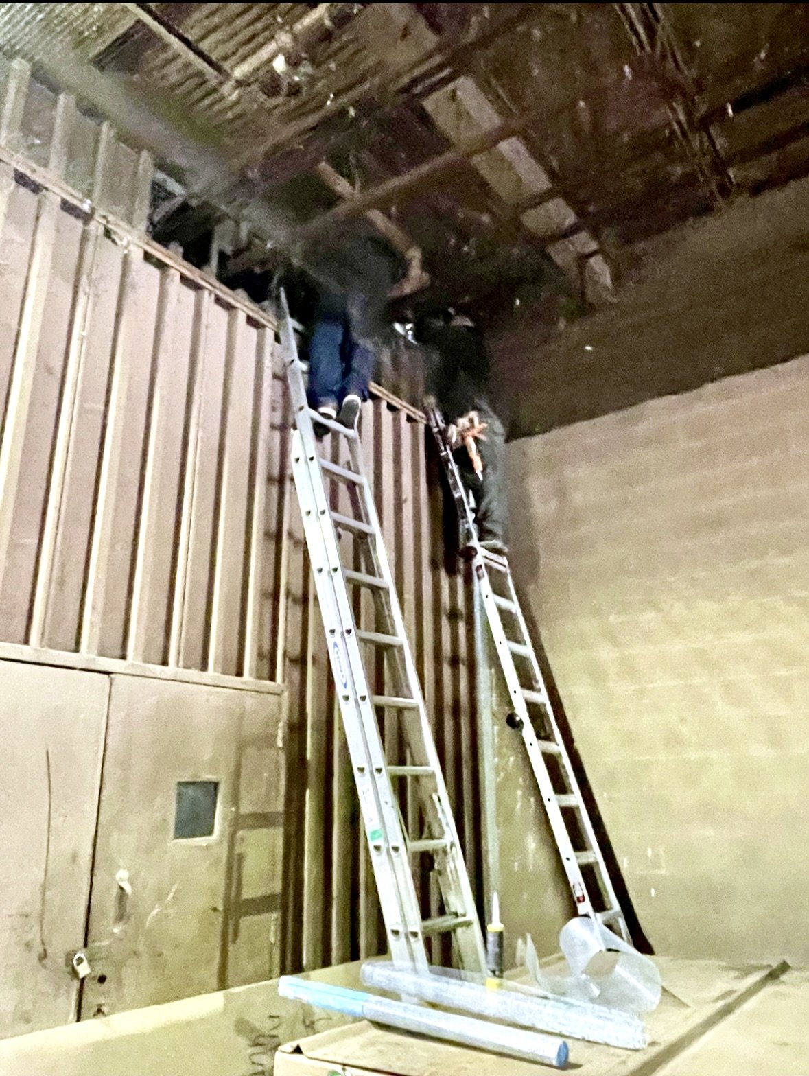 Two workers on ladders installing or repairing a ceiling in an unfinished room with visible wooden framing and drywall. performing rodent exclusion at commercial property