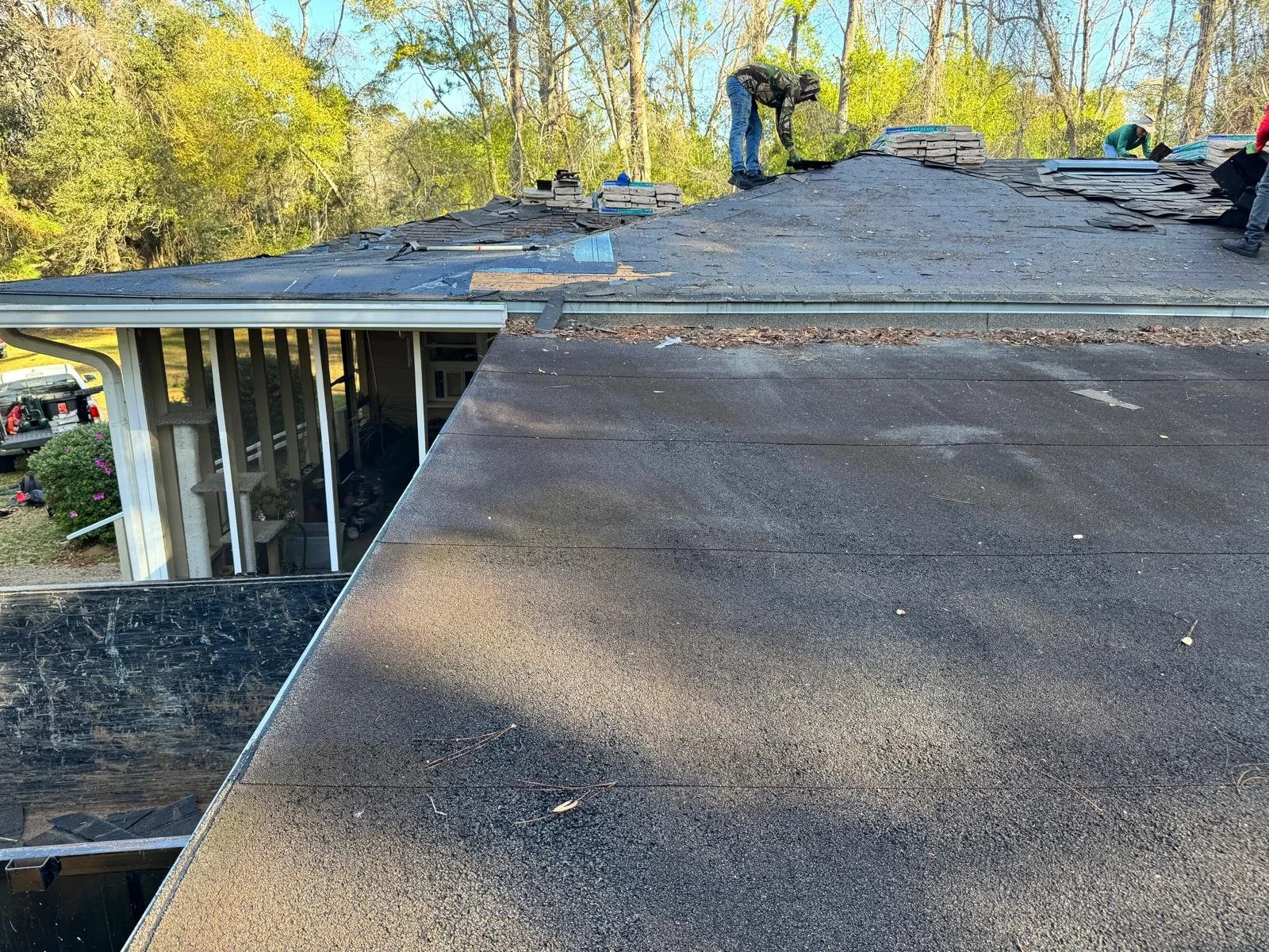 Workers repairing a house roof, with roofing materials on top and trees in the background.