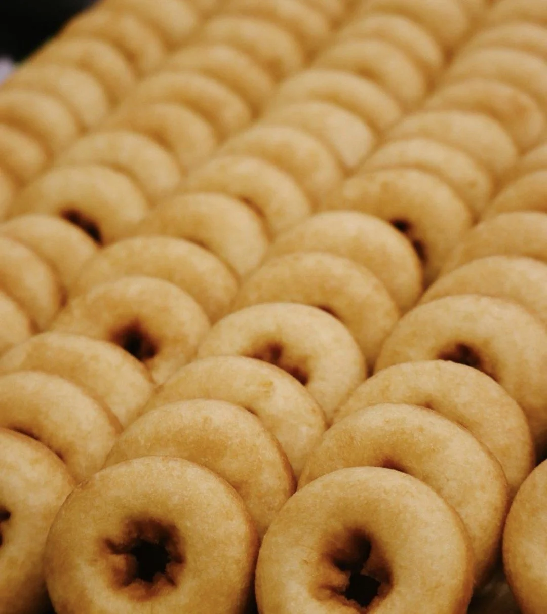 Close-up view of rows of yellow, donut-shaped cookies with a dark filling in the center.