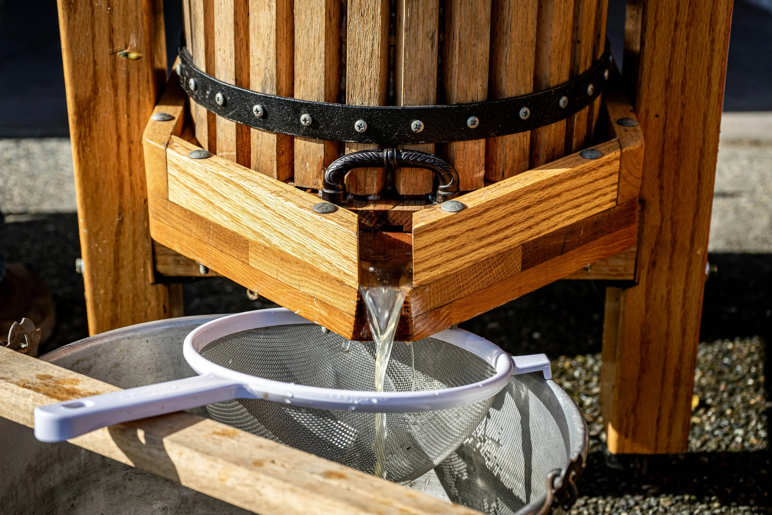 A bee hovering near a wooden honey extractor with water flowing into a white container below.