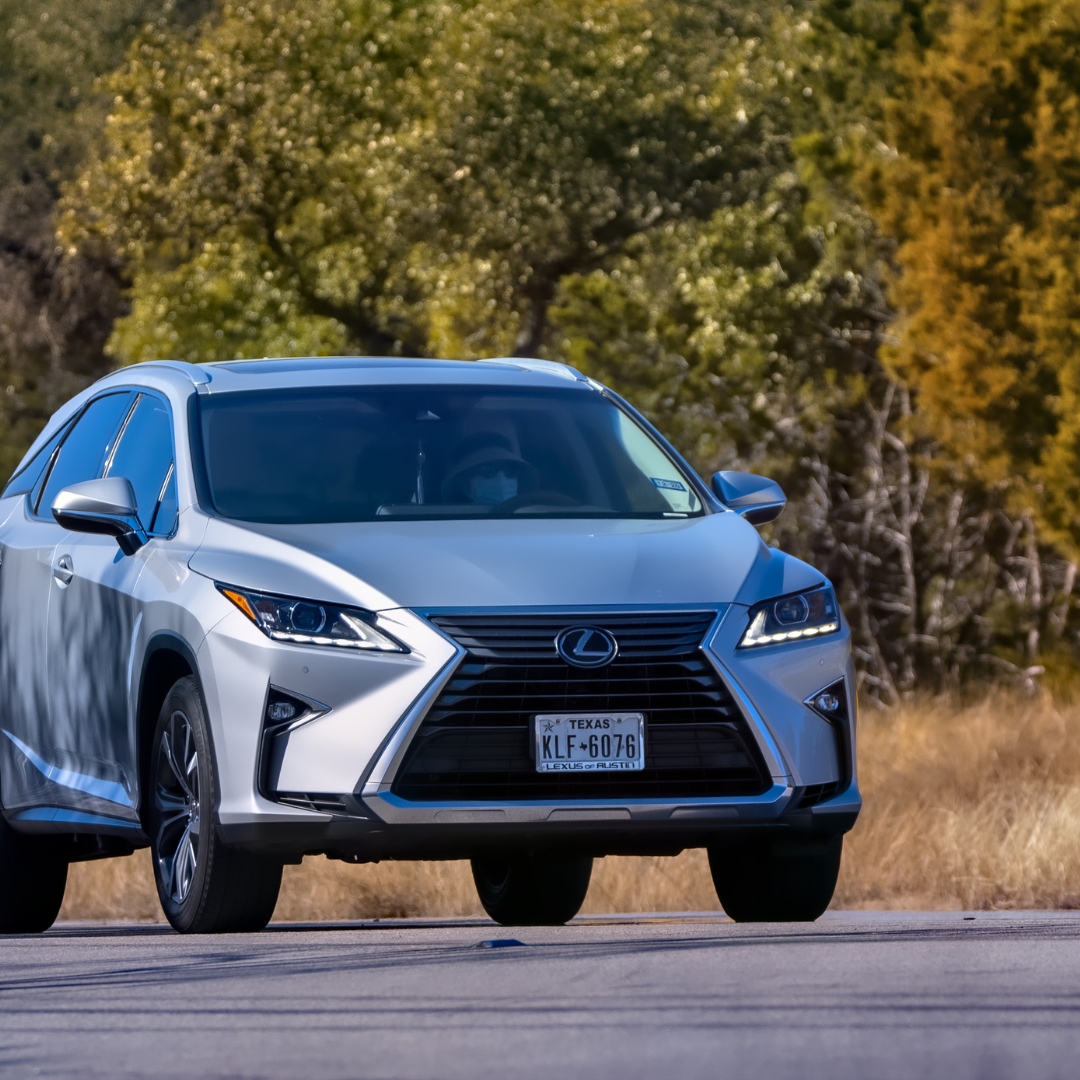 A silver Lexus RX driving on a rural road with trees in the background.