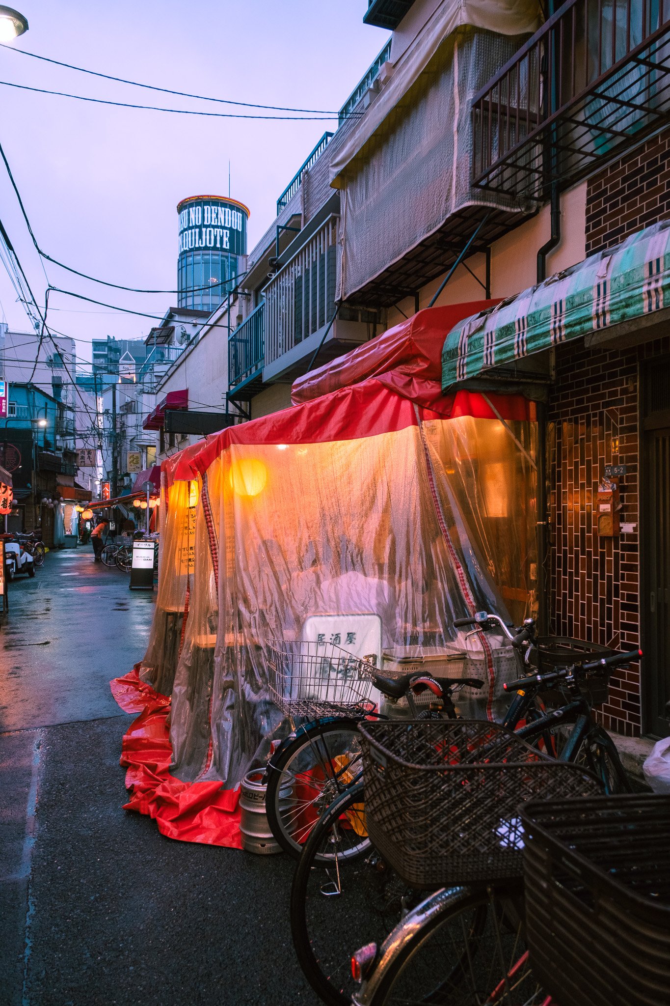Rainy Tokyo alley with bicycles and glowing restaurant lights.