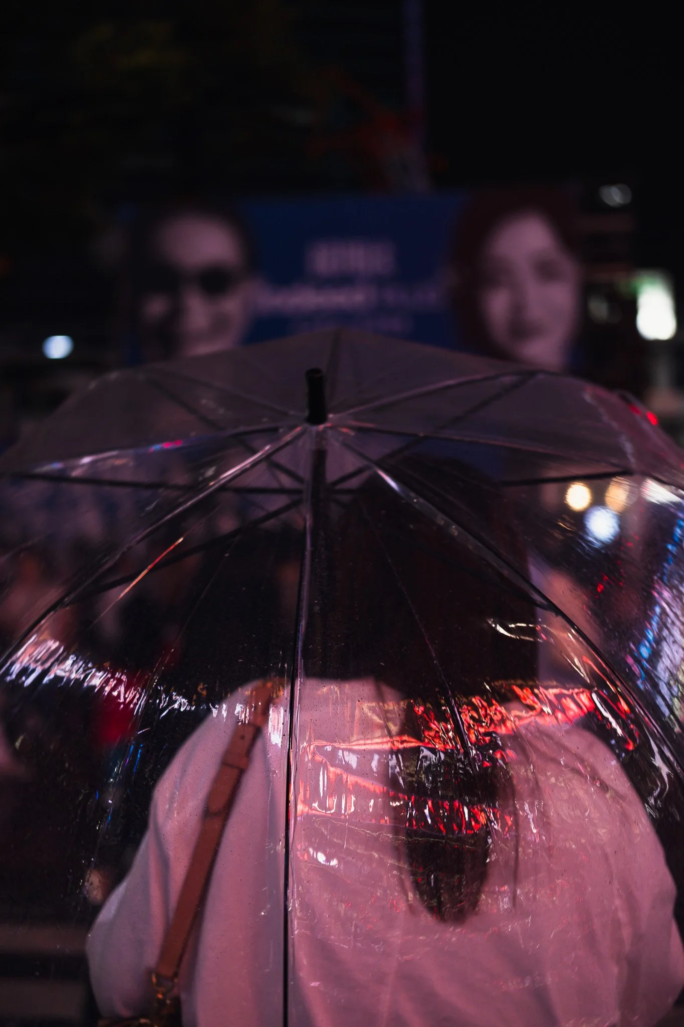 Transparent umbrella reflecting neon lights in rainy Tokyo streets.