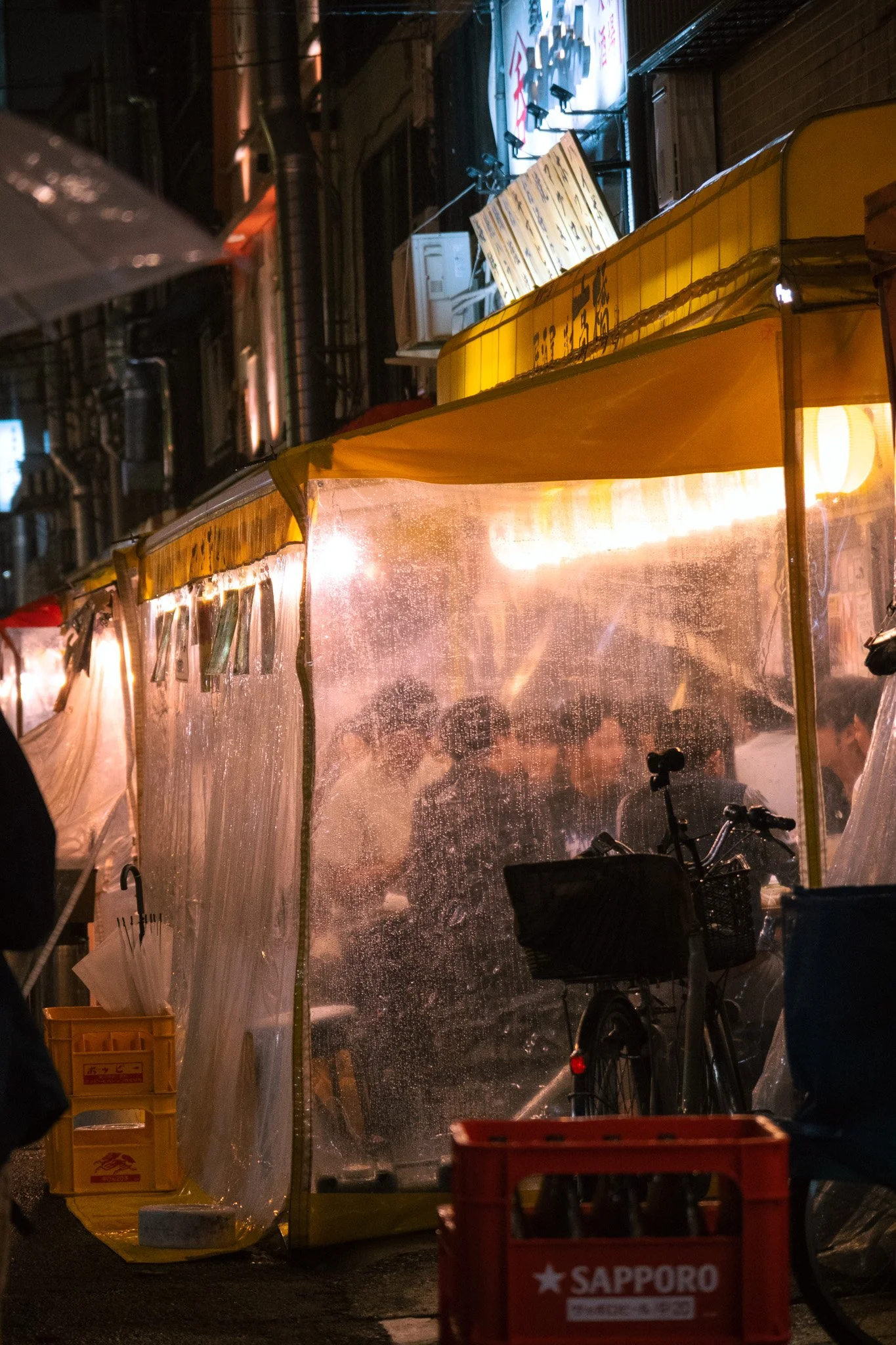 Rainy alley restaurant with warm lights in Tokyo nightlife district.