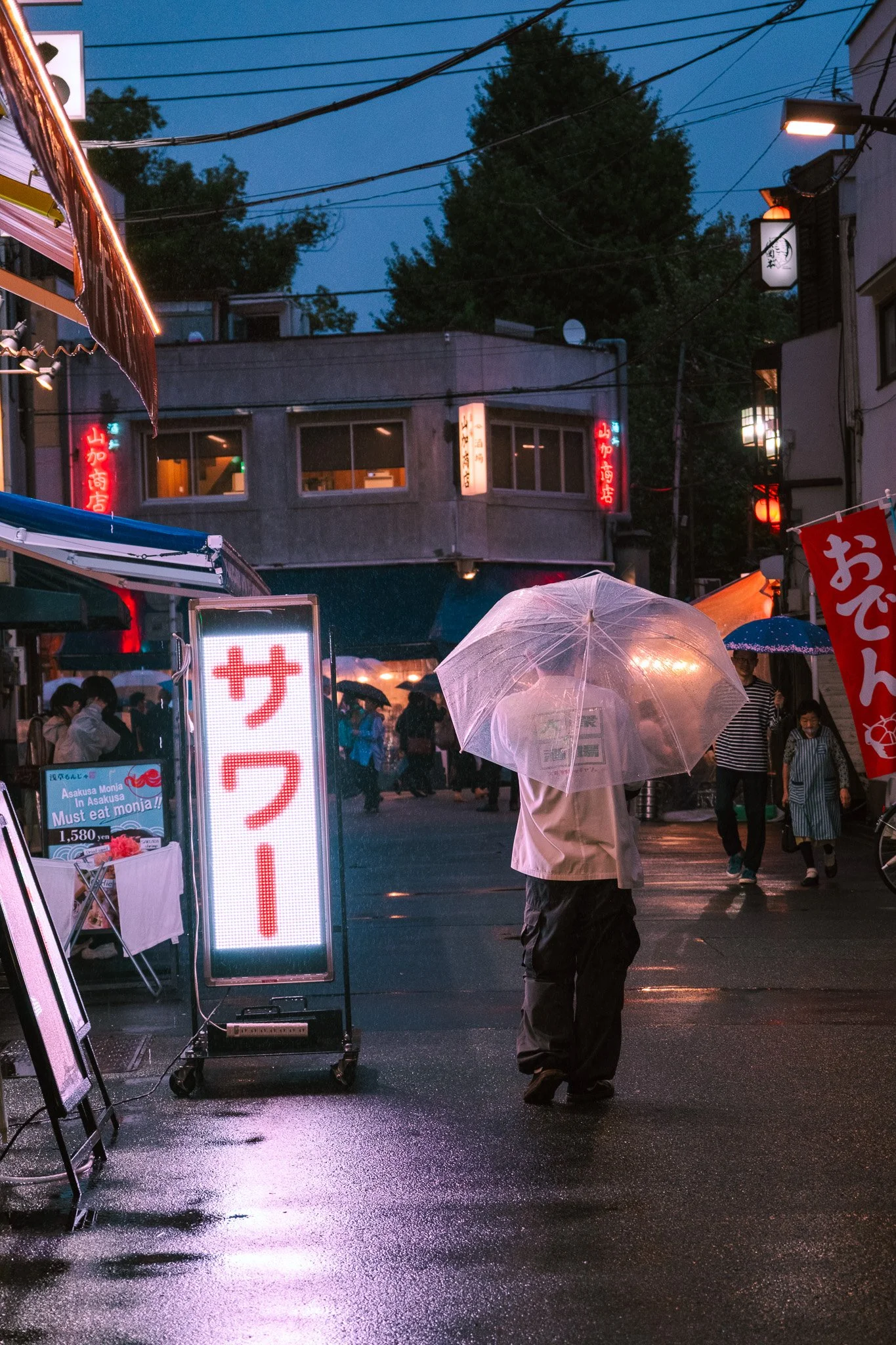 Person with transparent umbrella walking through Tokyo nightlife district.