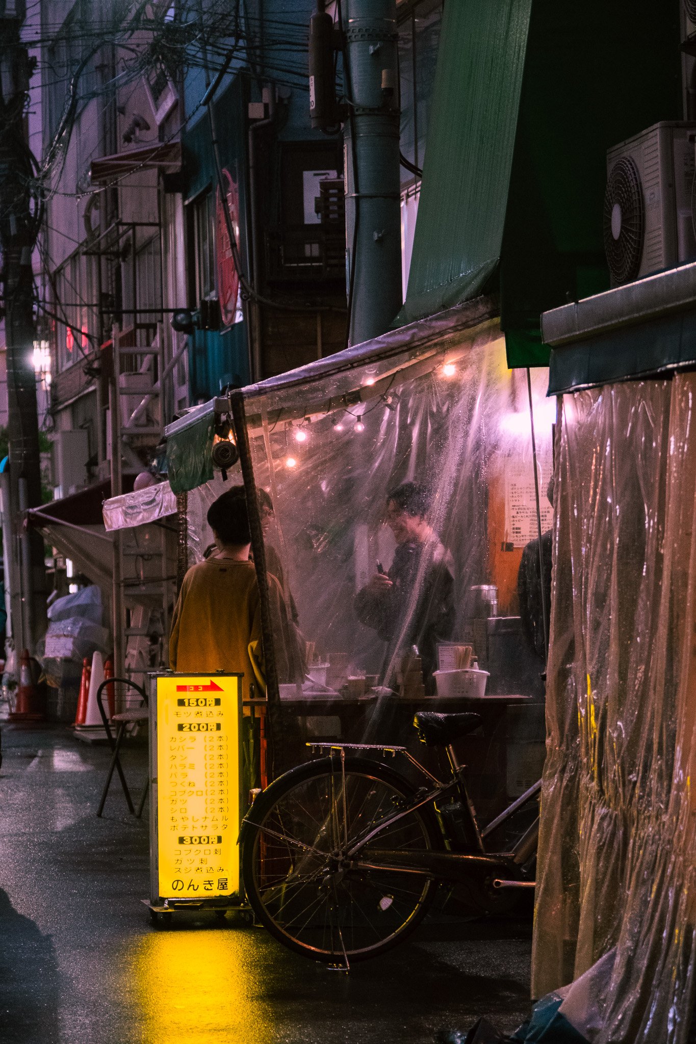 Rainy alley with small restaurants and bicycles in Tokyo at night.