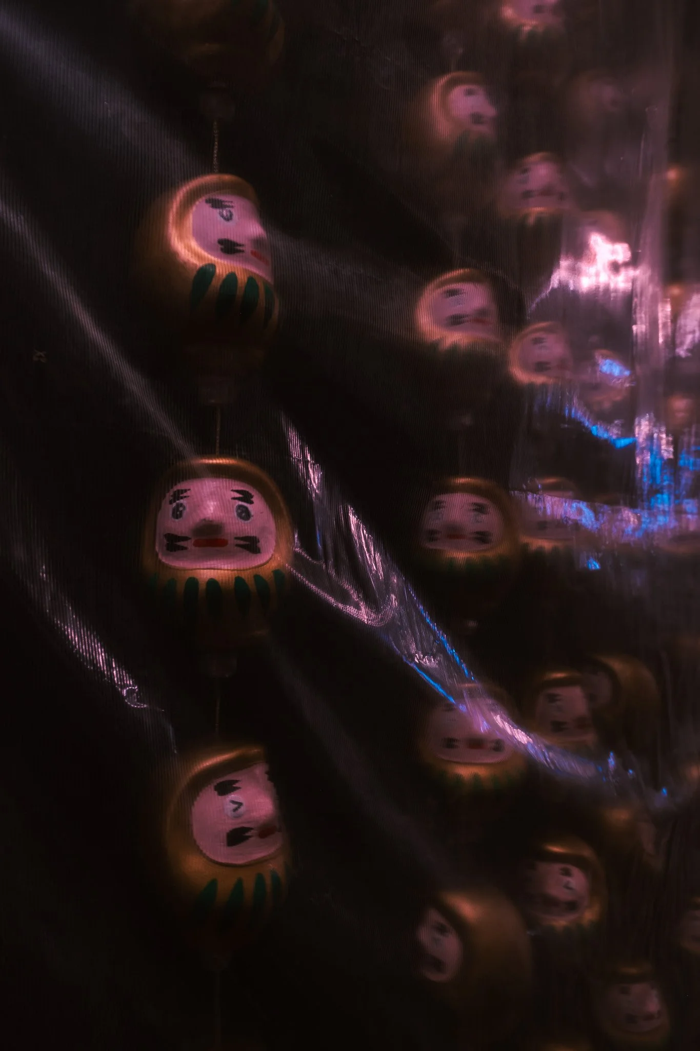 Daruma dolls reflected through plastic during a rainy Tokyo night.