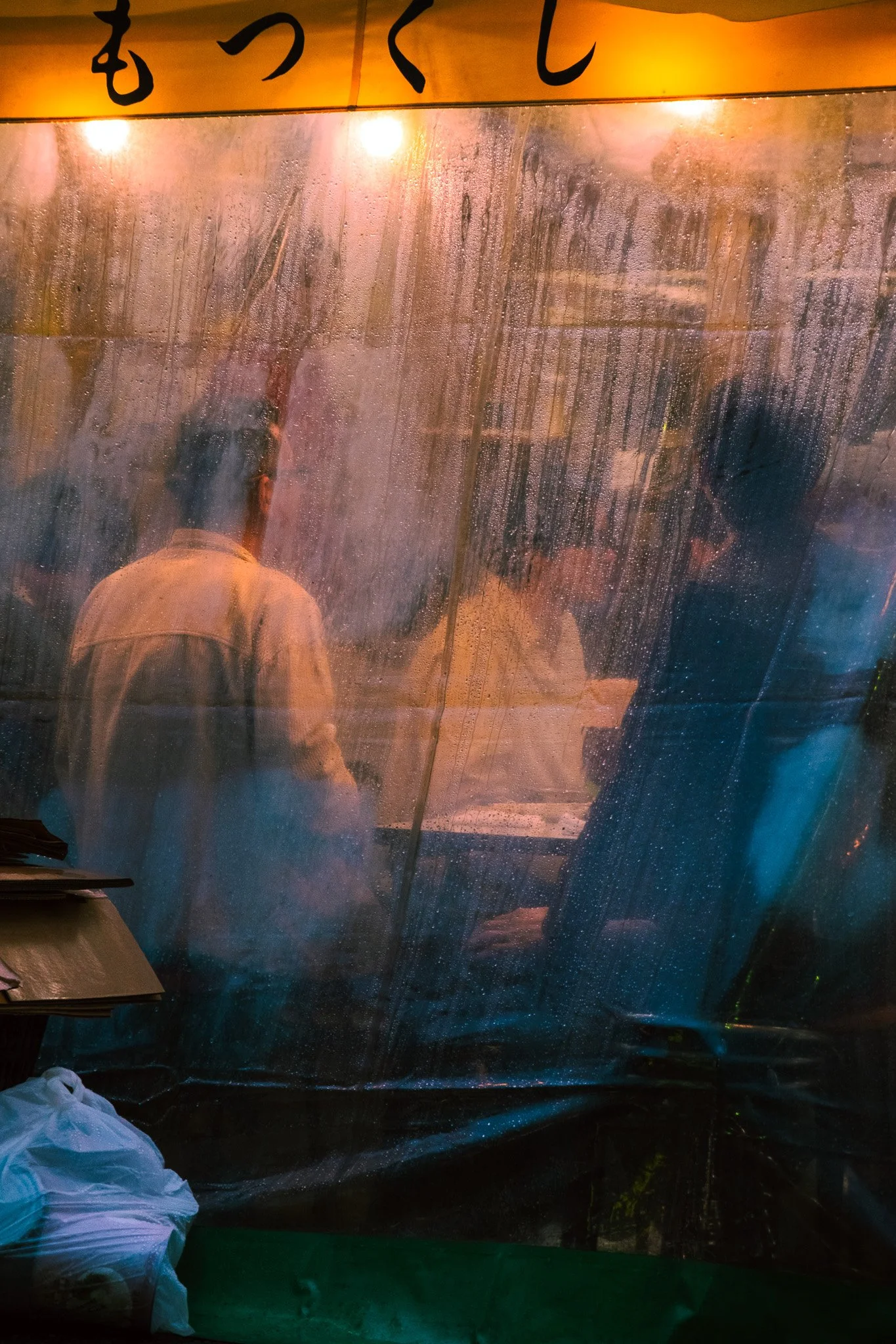 Blurred figures inside a Tokyo restaurant during a rainy evening.