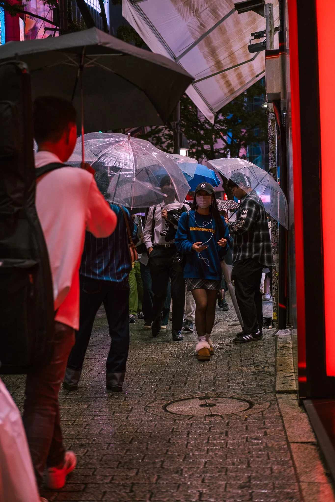 Pedestrians walking through a neon-lit rainy street in Tokyo, Japan.