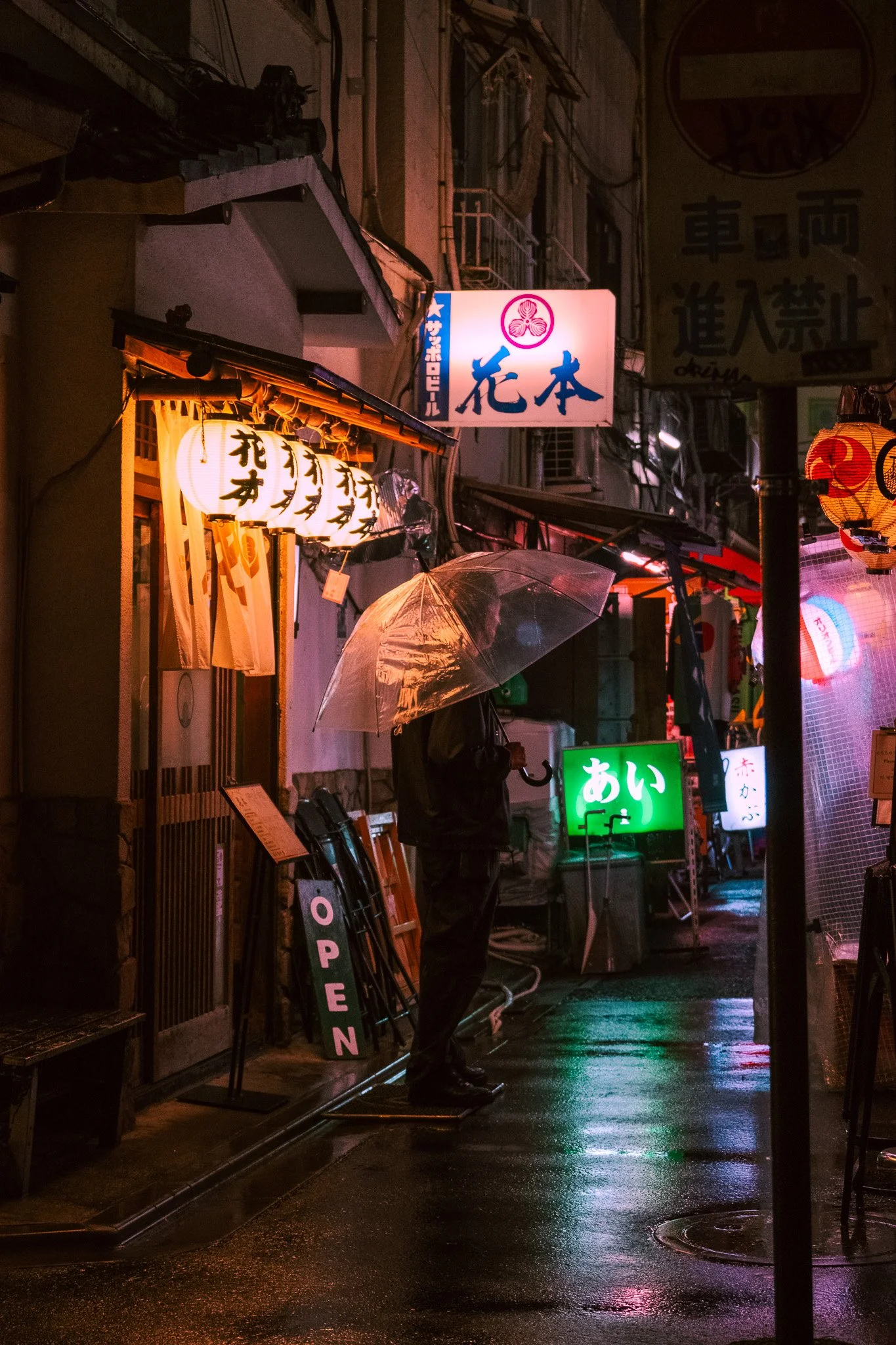 Person walking with umbrella through narrow Tokyo alley at night.
