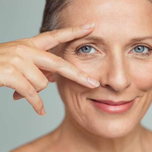 A woman with blue eyes makes a peace sign with her fingers near her face.