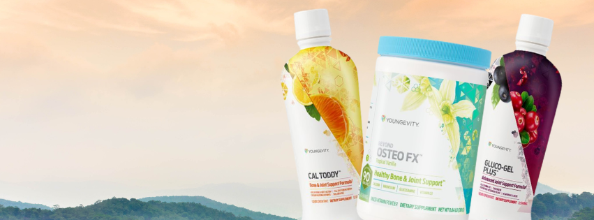Three bottles of dietary supplements with fruit labels against a sunset sky and distant mountains.